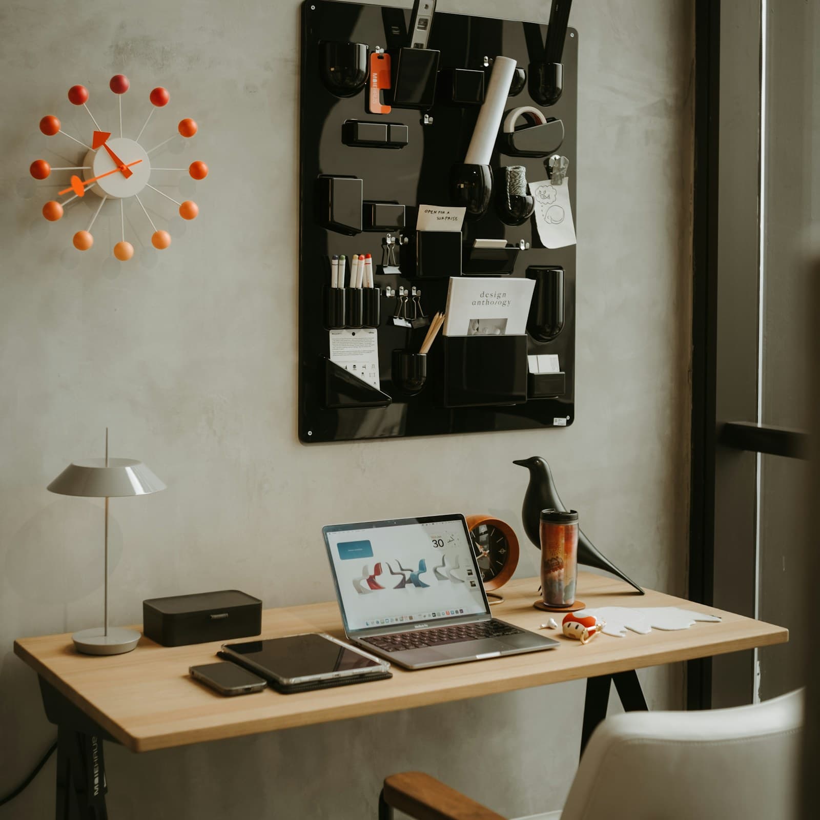 A tidy modern desk with an open laptop, a lamp and a wall organiser